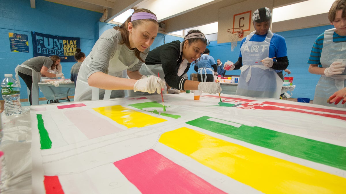 Amanda DeSenna (left) and Marielle Fortune paint one of the canvas squares that will make up Shira Walinsky's new mural, ''Migrating Home.'' (Jonathan Wilson for NewsWorks)