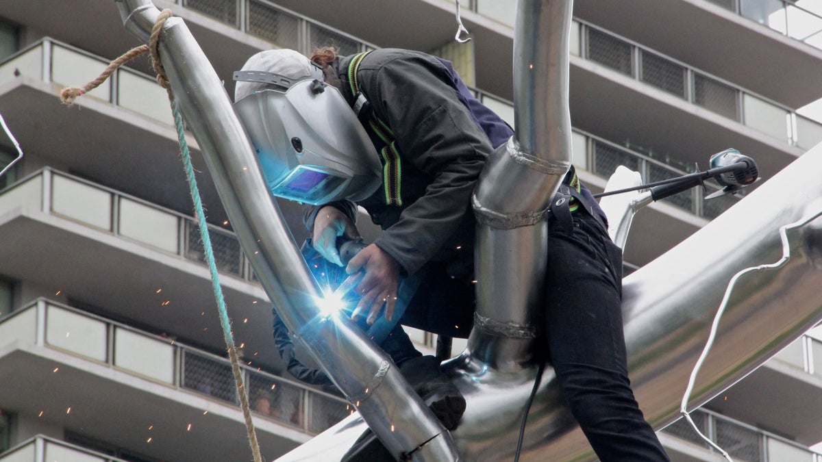  An installer welds a branch on Roxy Paine's 'Symbiosis.' The sculpture is on loan to the city for a year. (Emma Lee/WHYY) 