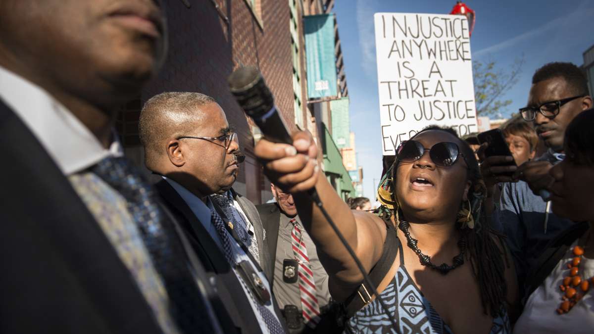 Erica Mines mockingly offers a microphone to a plainclothes officer outside of a Whole Foods on South Street. After interactions with the protestors took a turn for the ugly, the officer pictured refused multiple requests for his name and badge number. (Branden Eastwood for NewsWorks)