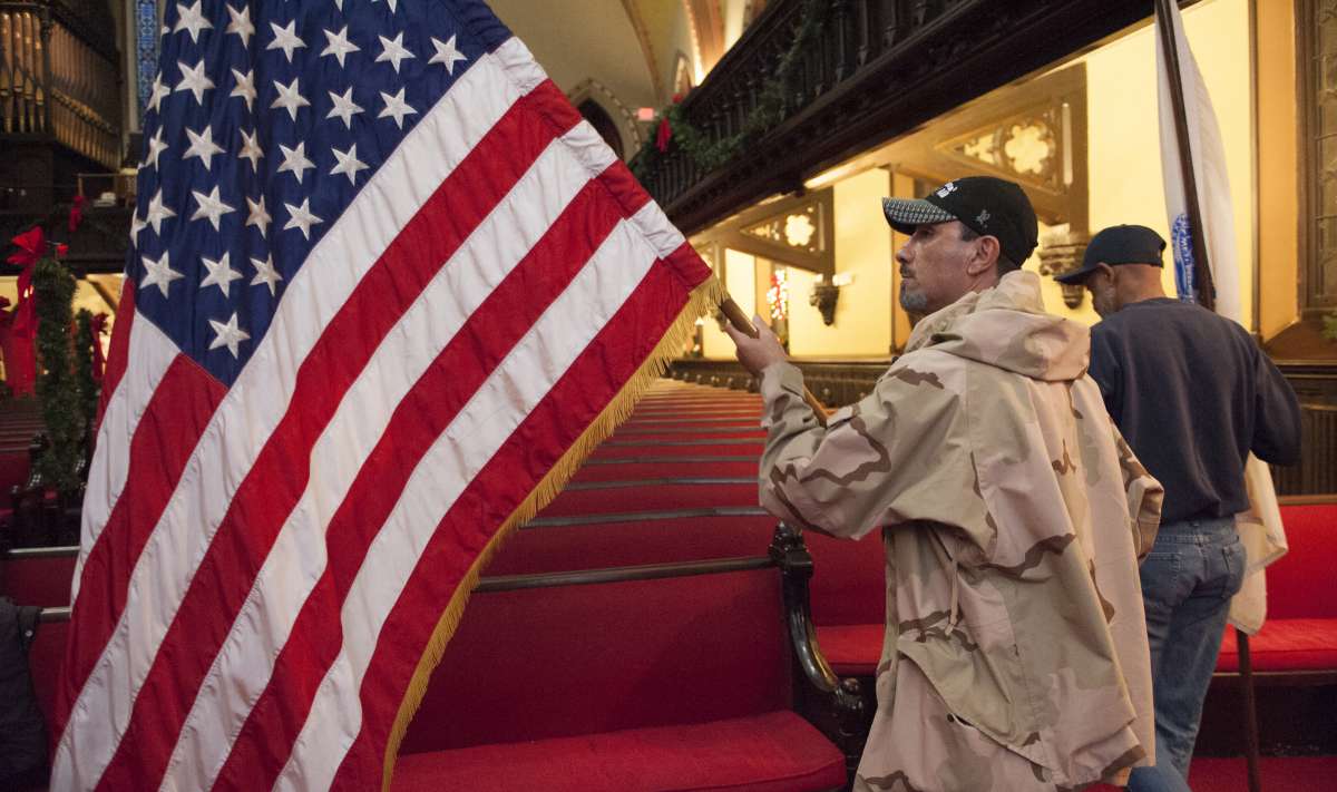 Benjamin Perez, a formerly homeless Army veteran unfurls the flag prior to the presentation of the colors at the Homeless Memorial Day service held at the Arch Street United Methodist Church in Center City. (Jonathan Wilson/for NewsWorks)