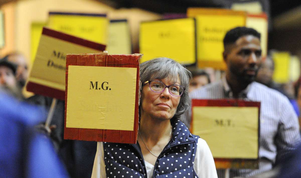 As the names of the deceased were read from the podium, participants rose from their seats holding the placards of homeless people who had passed away during the year. (Jonathan Wilson/for NewsWorks)