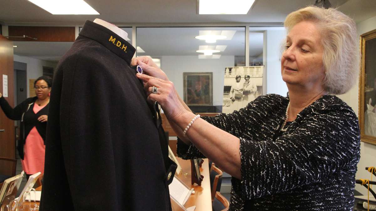 Dr. Jean Whelan, assistant director of the Barbara Bates Center for the Study of the History of Nursing, adjusts a pin on a Mercy Douglass nursing cape at the center's exhibit on the school, which trained black nurses for a segregated health care system. (Emma Lee/for NewsWorks)