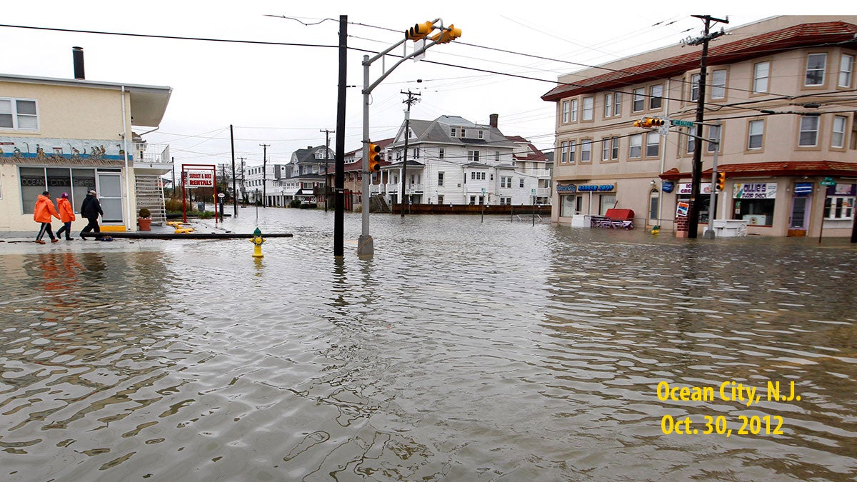  FILE - In this Oct. 30, 2012 file photo, people walk along a flooded intersection of 8th Street and Atlantic Avenue, in Ocean City, N.J., after the storm surge from Superstorm Sandy flooded much of the town. (AP Photo/Mel Evans, File) 