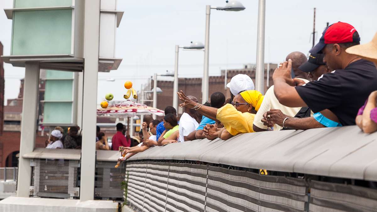 Kim Hopson (yellow dress) tosses fruit into the Schuylkill River during the Odunde Festival. Hopson says the offerings are a way of giving thanks for the blessings of the past year and a way of asking for more in the coming year. (Brad Larrison/for NewsWorks)