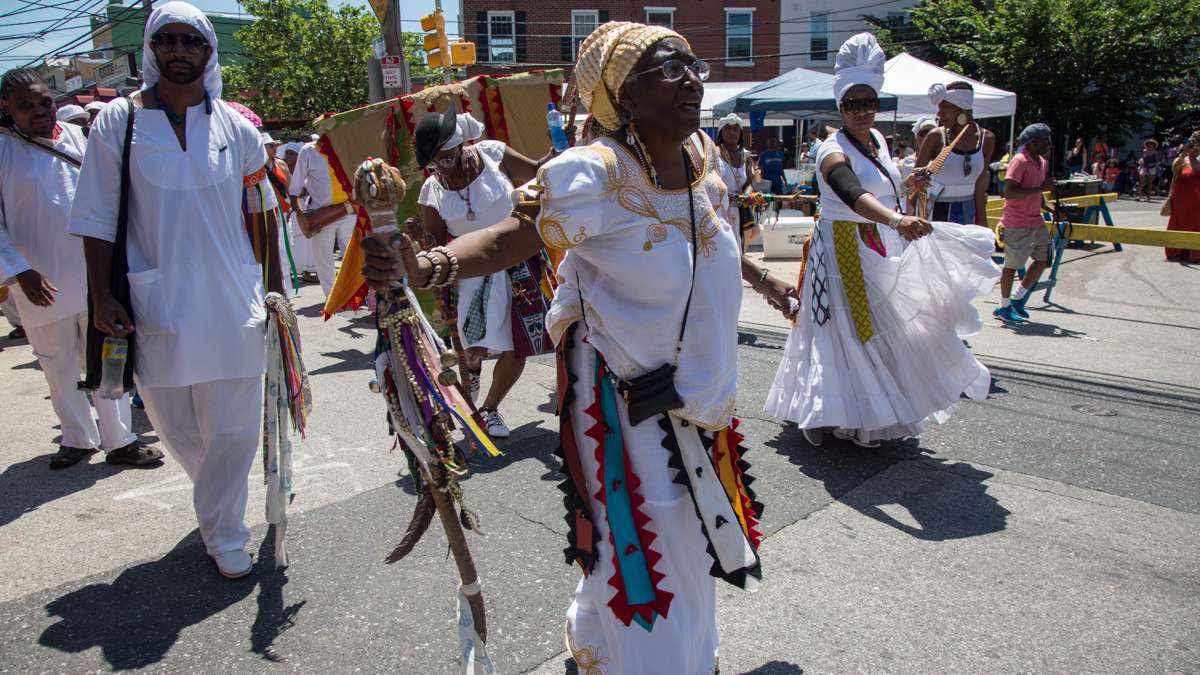 E Iya Olakunle Olundia (center) leads the procession toward the Schuylkill River to bring offerings to the Yoruba river goddess at the opening of the Philadelphia Odunde Festival. Dancers in white surround the two costumed dancers to protect the spirits of their ancestors.