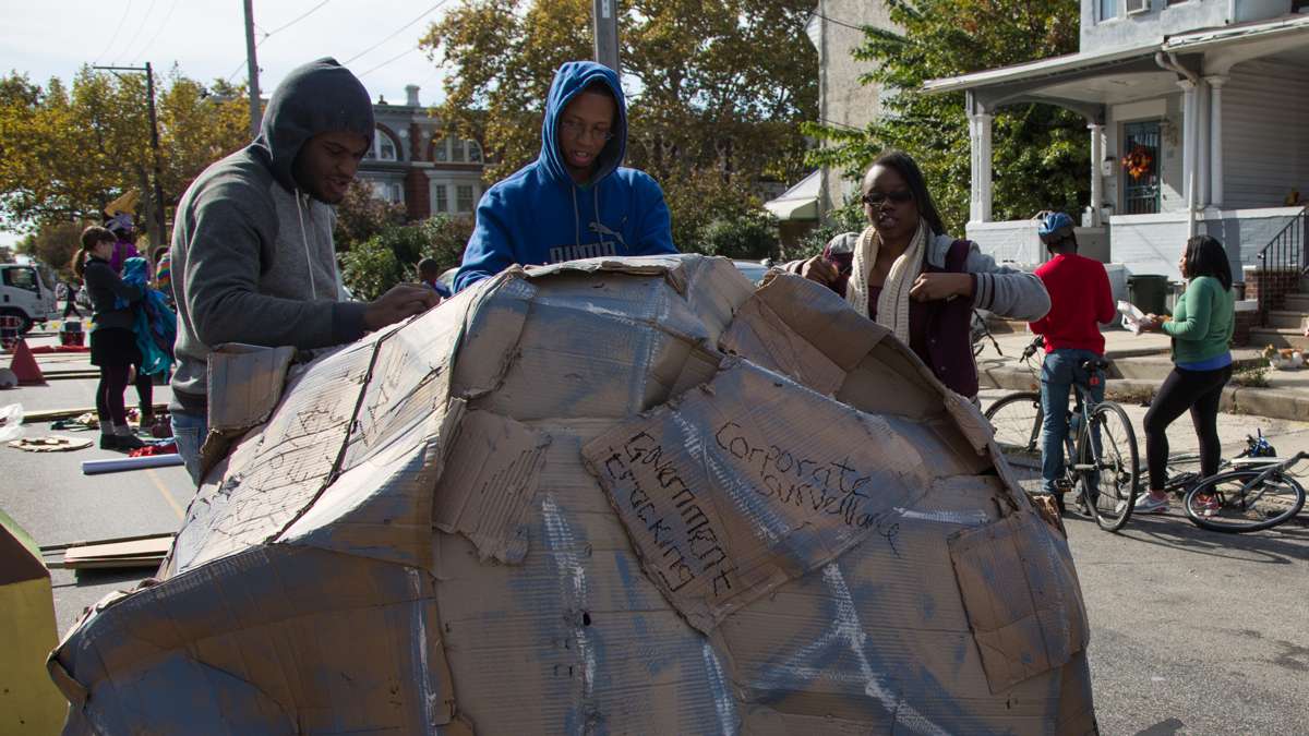 Teenagers from the Youth Volunteer Corps cover a cardboard boulder with different types of injustice before the start of the 17th annual Peoplehood parade in West Philadelphia, October 29th 2016. (Emily Cohen for NewsWorks)