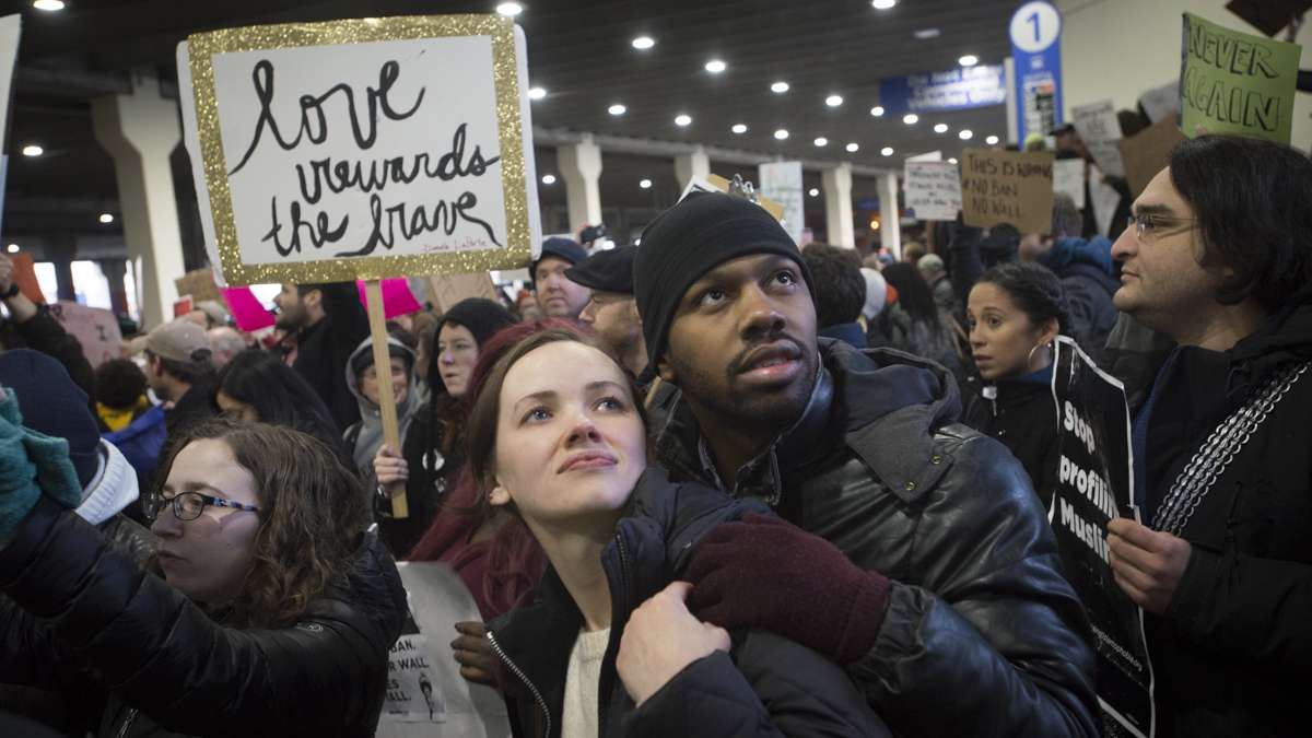 Leigh Wilson (left) and Nate Hall read signs at the protest against Donald Trump’s executive order on immigration. Wilson says this is her fourth protest opposing Trump. (Branden Eastwood for NewsWorks)