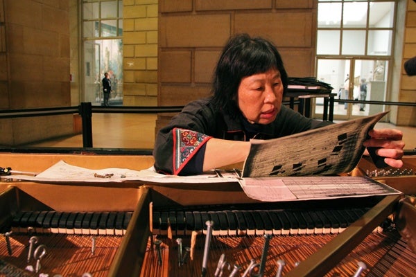 <p>Margaret Leng Tan consults the instructions for preparing a piano for a John Cage Competition. Bolts, screws, and bits of wood and rubber are arranged among the strings. (Emma Lee/for NewsWorks)</p>
