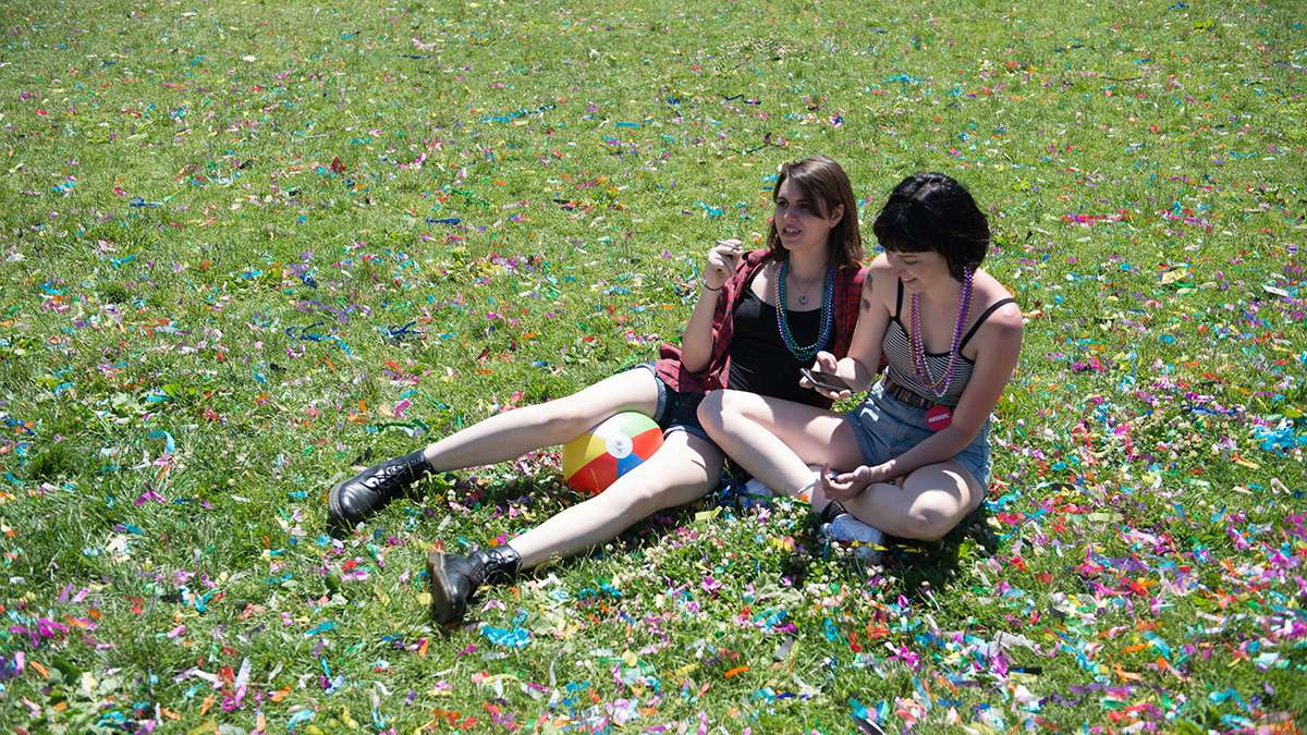 Laura Foley and Ella Anderson sit in confetti filled grass near Independence Hall. (Branden Eastwood for NewsWorks)