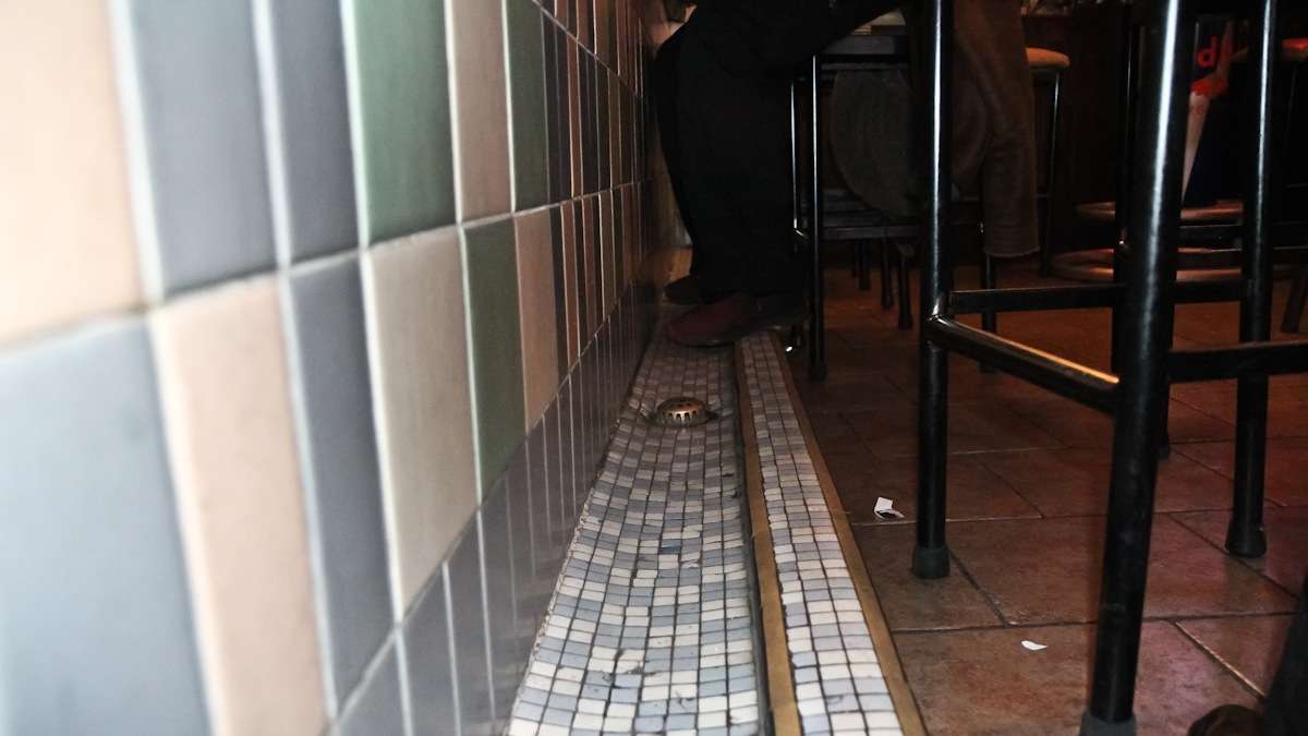 Owner Lou Capozzoli explains a bar's gutter-like trough was used for spitting and draining. (Kimberly Paynter/WHYY)