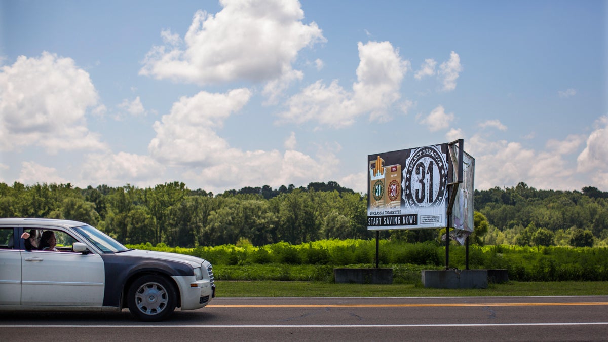  A billboard advertises discounted cigarettes adjacent to a field used to grow tobacco on the Seneca Nation's Cattauragus reservation in Western New York. (Photo by Jessica Kourkounis/for WHYY)  