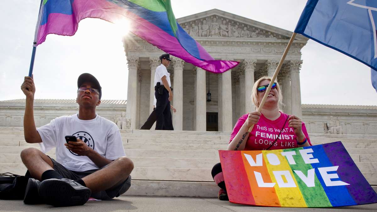  Carlos McKnight, 17, of Washington, (left), and Katherine Nicole Struck, 25, of Frederick, Md., hold flags in support of gay marriage as security walks behind outside of the Supreme Court in Washington, Friday June 26, 2015. (Jacquelyn Martin/AP Photo) 