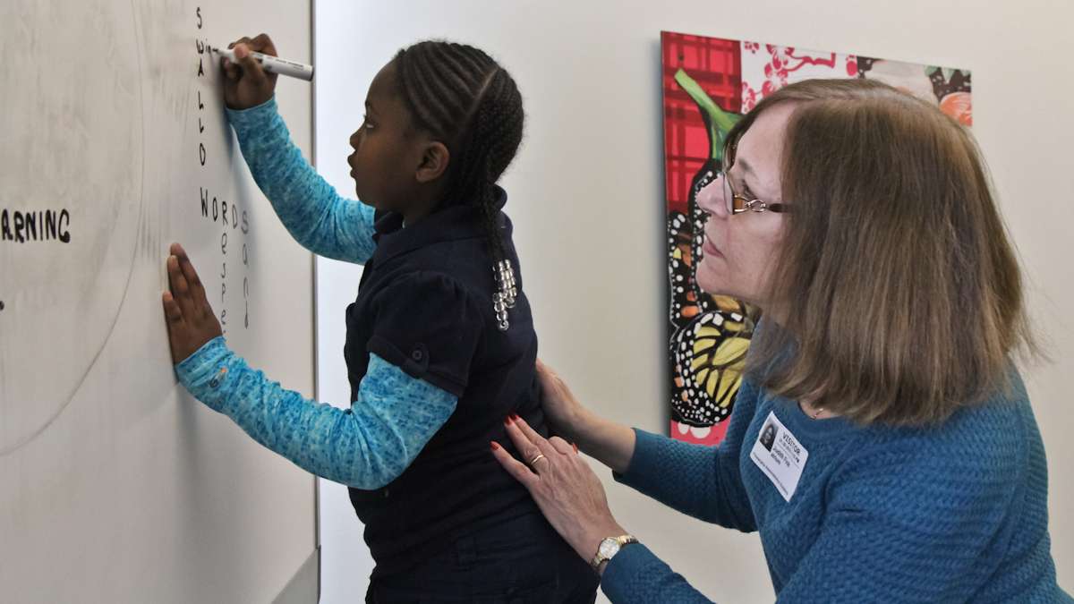 Retired Philadelphia teacher Judith Fink helps Jayairra Fox, 7, add ‘window’ to the board. (Kimberly Paynter/WHYY)