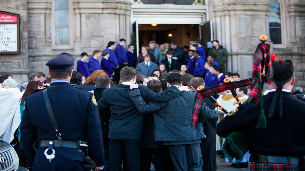 Mourners lock arms outside of Saint John the Baptist Roman Catholic Church following a funeral mass for Shane Montgomery. (Brad Larrison/for NewsWorks)