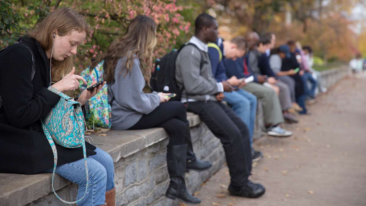 Emily Flanigan (far left), a Junior studying mechanical engineering at Penn State, waits at a bus stop with other students on College Avenue. (Lindsay Lazarski/WHYY)