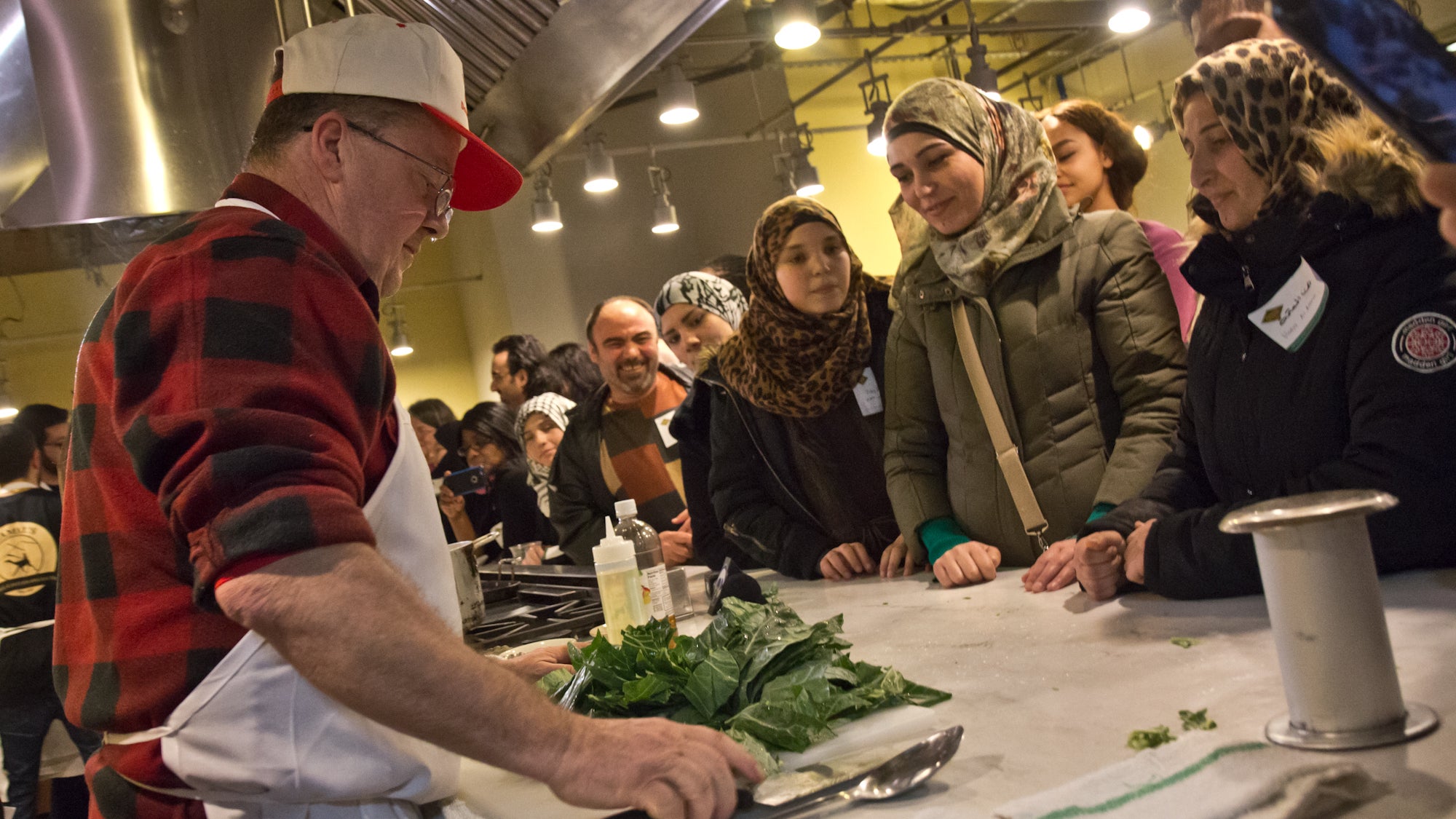 The Down Home Diner’s chef, Jack McDavid, demonstrates how to prepare collard greens at the Reading Terminal Market meal for Syrian refugees and Mayfair residents. (Kimberly Paynter/WHYY)