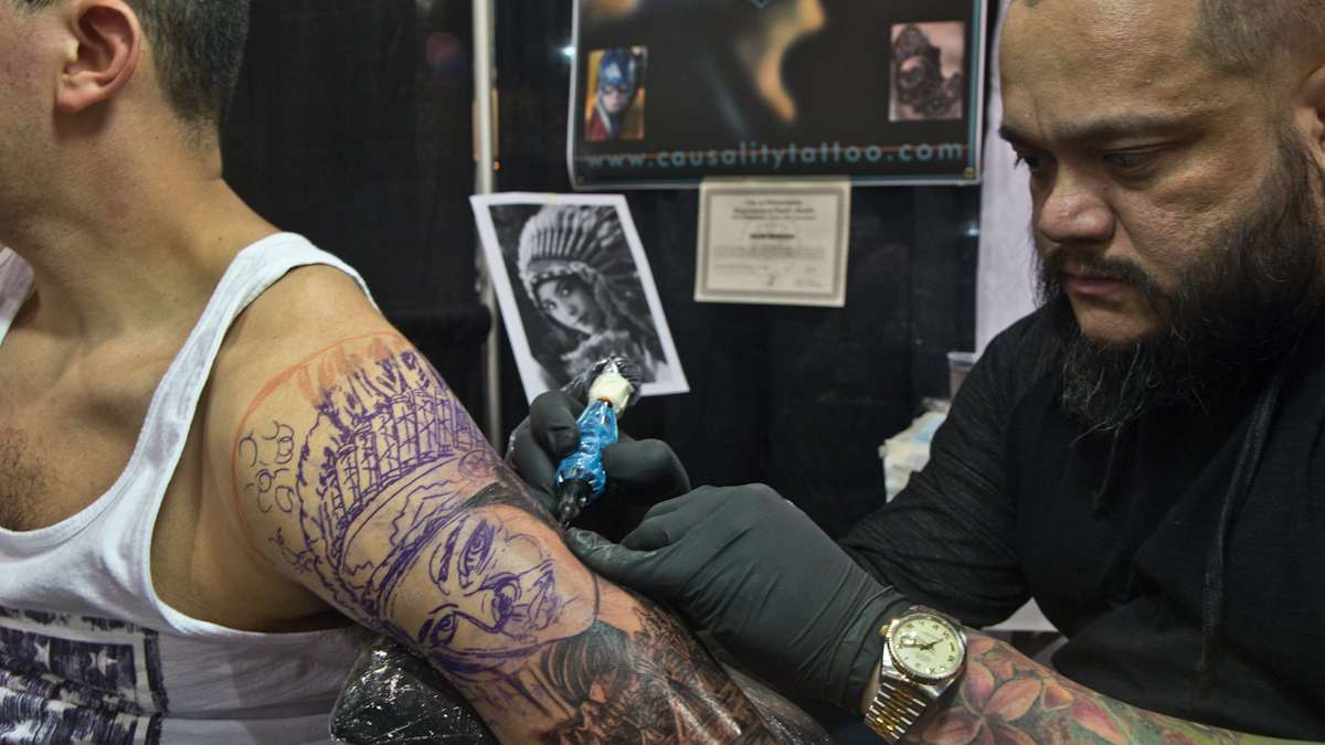 Artist Javier Eastman tattoos a portrait of a native girl on Jose Restrepo, a fan of Eastman’s work. (Kimberly Paynter/WHYY)