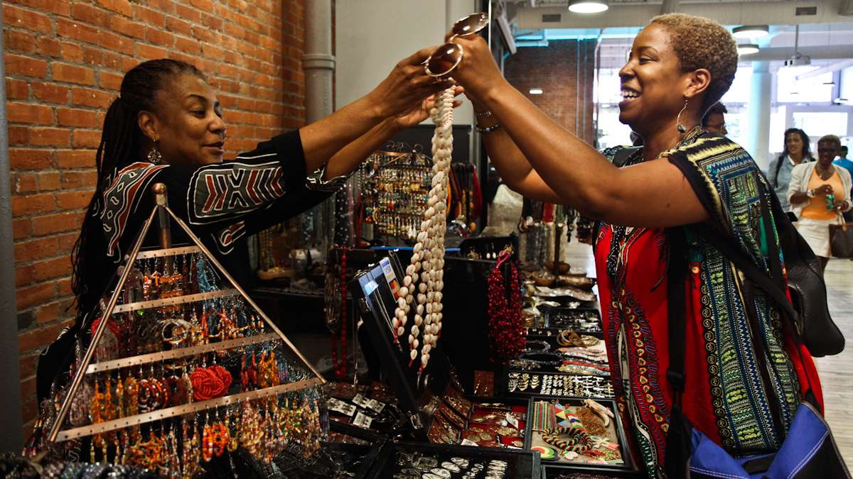 Rashida Watson (left) gives Jasmine Burnett, Deputy Director of New Voices for Reproductive Justice, a shell necklace to try on. (Kimberly Paynter/WHYY)