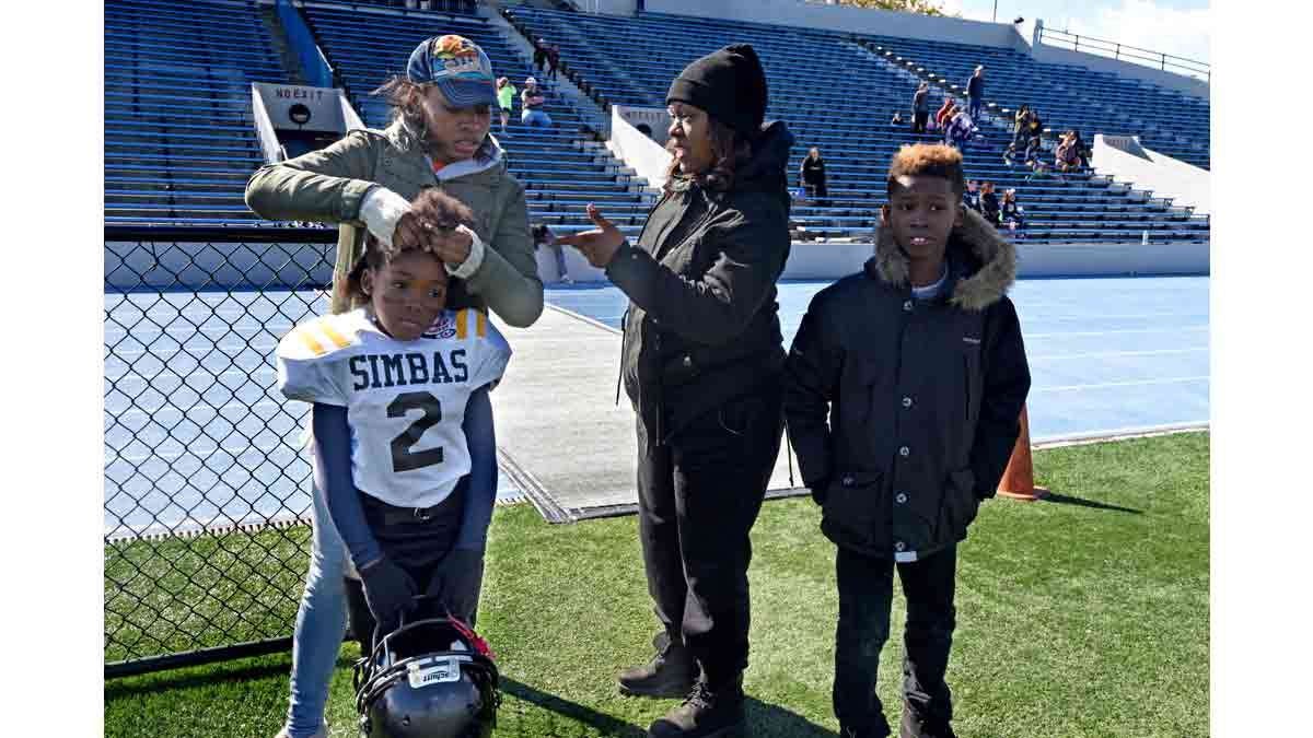 During the last game of the season in Asbury Park, Jasmine Skinner braids Janiyah Hill's hair closer to her scalp so her helmet will fit better; at right is Hill's mother, Renekia Robinson and Hill's brother, Izayah Hil, 10.
