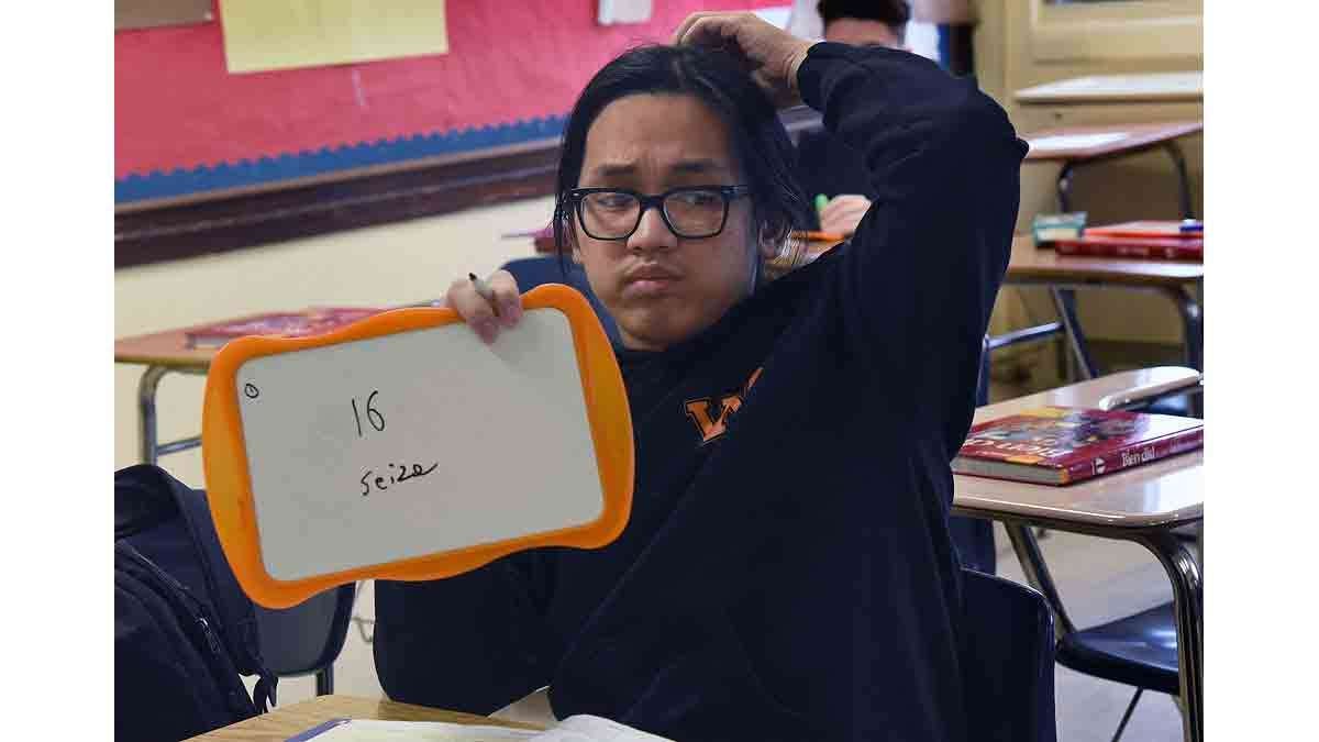 Minh Le, 16, holds up an answer in Saillard's French class during a lesson on numbers.