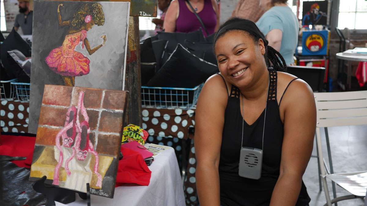 Artist sits with some of her paintings. (Evelyn Tu/for NewsWorks)