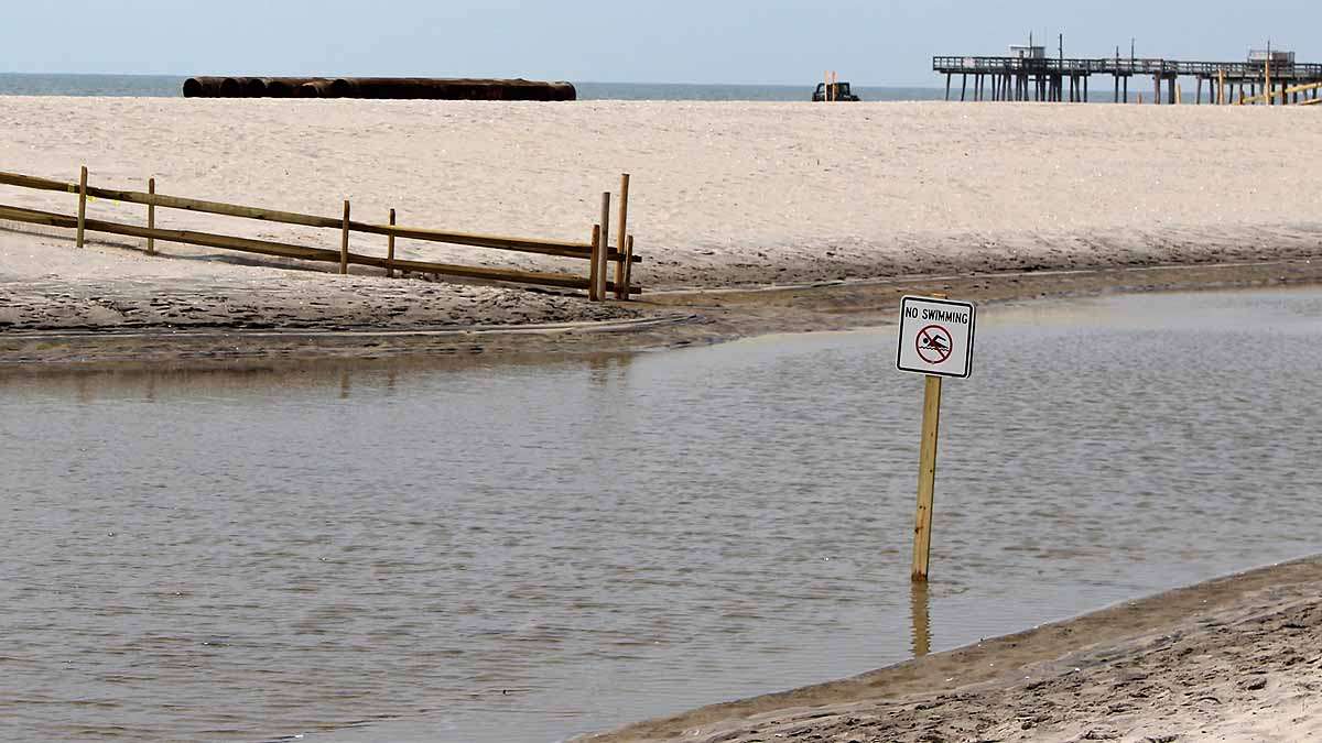 A no swimming sign sits in a pool of dirty water after this weekend's heavy rainfall.