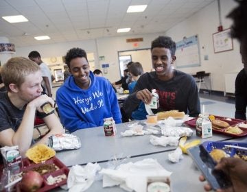 Abdiaziz Shaleh, right, a Lewiston high school senior and co-captain of the soccer team, and Essa Gedi, center, both whose families emigrated from Somalia, sit with classmate Isiah Leach, left, during lunch in the school's cafeteria in Lewiston, Maine, Wednesday, March 15, 2017. Two years ago, immigrant children led the high school soccer team to win the state championship, a moment heralded as a triumph for the city's embrace of its immigrant community. (AP Photo/David Goldman)