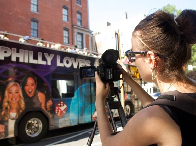 Student behind a camera filming a bus