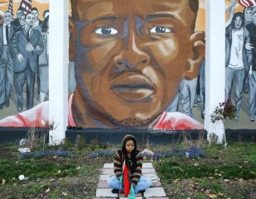  In a Dec. 16, 2015 file photo, Jazmin Holloway sits below a mural depicting Freddie Gray at the intersection of his arrest, in Baltimore. (Patrick Semansky/AP Photo, File) 