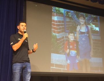 Top NASCAR racer Kyle Larson addresses students Tuesday at t St. Georges Technical High School while a photo with his sister from his youthful racing days is projected on a screen. (Cris Barrish/WHYY)