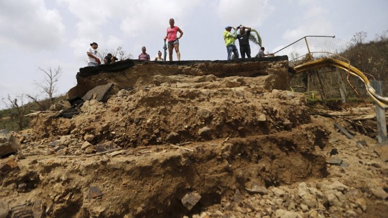 Residents Wednesday look over the edge of a bridge that was swept away by Hurricane Maria