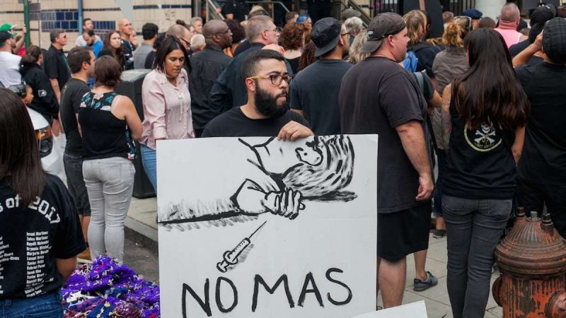 Aaron Cruz holds a sign calling for no more overdoses at the March in Black through Kensington Thursday evening. (Brad Larrison for NewsWorks)