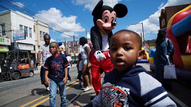 A young man dressed as Mickey Mouse plays with neighborhood children on Woodland Avenue. (Annie Risemberg for NewsWorks)