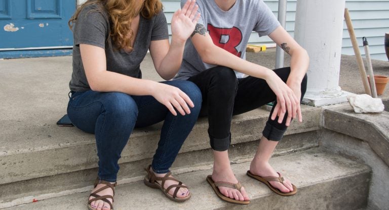 Two students sit on the front porch at one of the three 