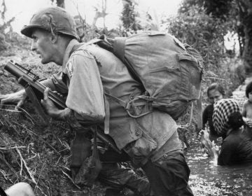  In this Jan. 1, 1966, file photo, a paratrooper of the 173rd U.S. Airborne brigade crouches with women and children in a muddy canal as intense Viet Cong sniper fire temporarily pins down his unit near Bao Trai in Vietnam. (AP Photo/Horst Faas, file) 