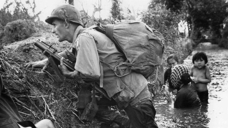  In this Jan. 1, 1966, file photo, a paratrooper of the 173rd U.S. Airborne brigade crouches with women and children in a muddy canal as intense Viet Cong sniper fire temporarily pins down his unit near Bao Trai in Vietnam. (AP Photo/Horst Faas, file) 