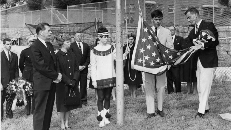 A flag that draped casket of John M. Cole, Jr., a Roxborough High School graduate who died in Vietnam, is unfurled during a May 26, 1967, memorial service on the school athletic field by Paul Cottone, student body president, and Robert Bunch (right), a faculty advisor. Cole's parents, Mr. and Mrs. John M. Cole, are at left. Their daughter, Donna, a member of the school drill team, waits to raise the flag. (Charles T. Higgins / Courtesy of George D. McDowell Philadelphia Evening Bulletin Collection, Temple University Libraries)