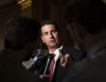 Man in suit at microphone, background darkened around him