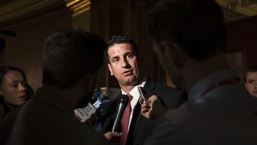 Man in suit at microphone, background darkened around him