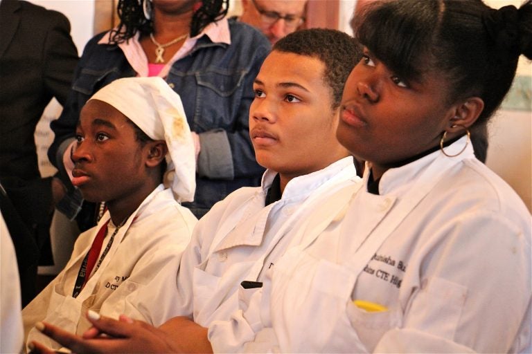 Students dressed in chef's whites listen during an assembly.