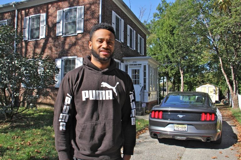 Kenneth Hammon stands in front of his brick town house in Camden. There is a Mustang car in the driveway