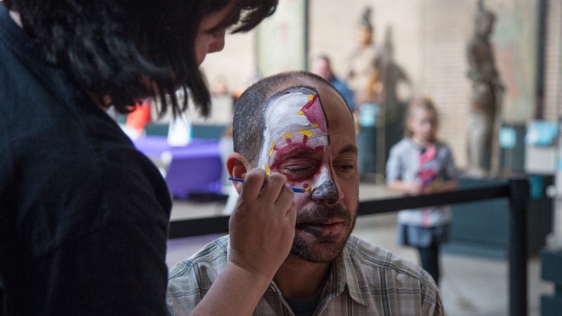 A woman man paints half of a man's face to look like a skull