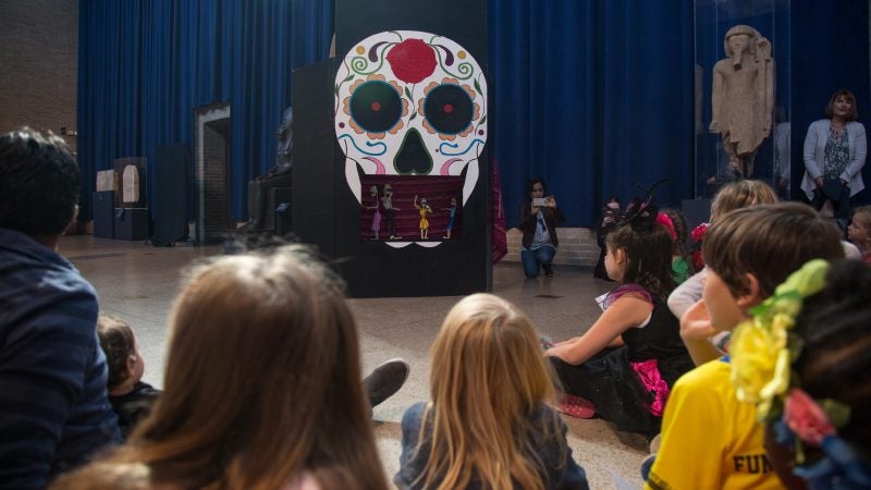 Children and adults gather to watch a marionette puppet show explaining the celebrations around Dia de los Muertos at Penn Museum's annual Day of the Dead celebration October 28, 2017. (Emily Cohen for WHYY)