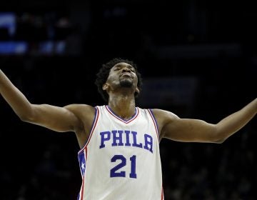 7 feet 2 inch- basketball star, Joel Embiid, number 21, in Sixers uniform, arms spread wide, looking up