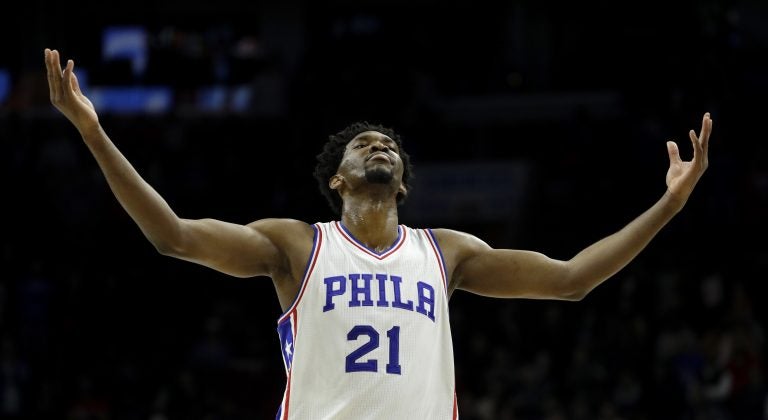 7 feet 2 inch- basketball star, Joel Embiid, number 21, in Sixers uniform, arms spread wide, looking up