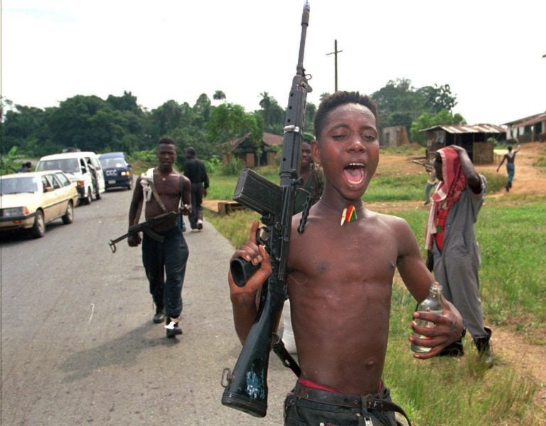 A child soldier; intoxicated and shirtless, holds a rifle