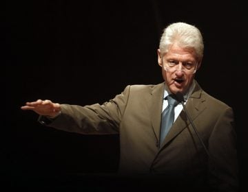 Bill Clinton, olive suit, arm outstreched gesturing, black background