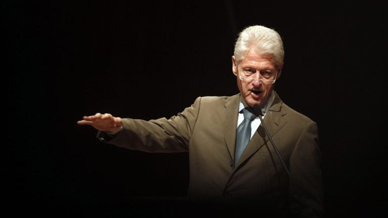 Bill Clinton, olive suit, arm outstreched gesturing, black background