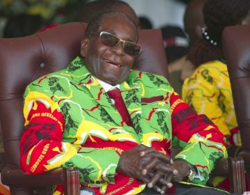 Zimbabwean President Robert Mugabe sits in a chair, sunglasses and a smile, wearing a colorful yellow, red, and green jacket