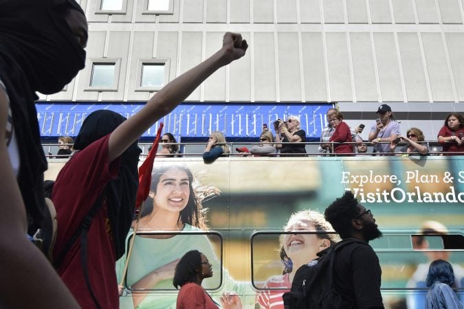A person holds up a fist in protest as tourists pass by on a double-decker bus